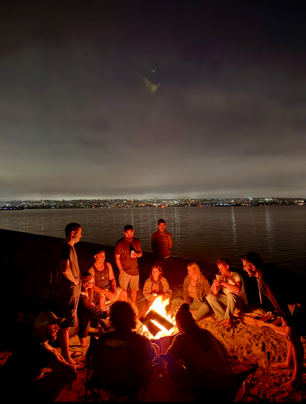 Friends gathered around a bonfire on the bay at night