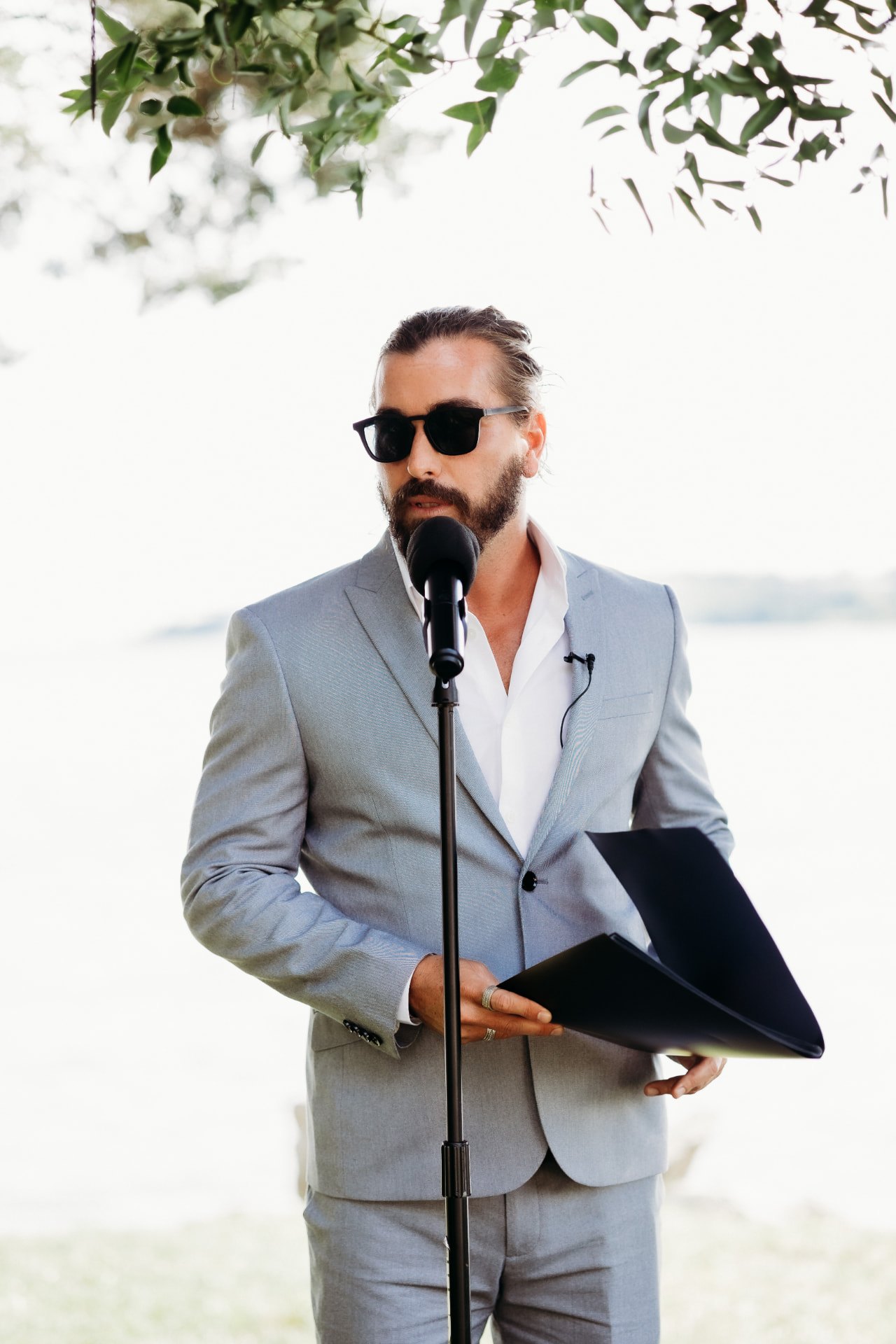 Speaking into a microphone at an outdoor ceremony by the water